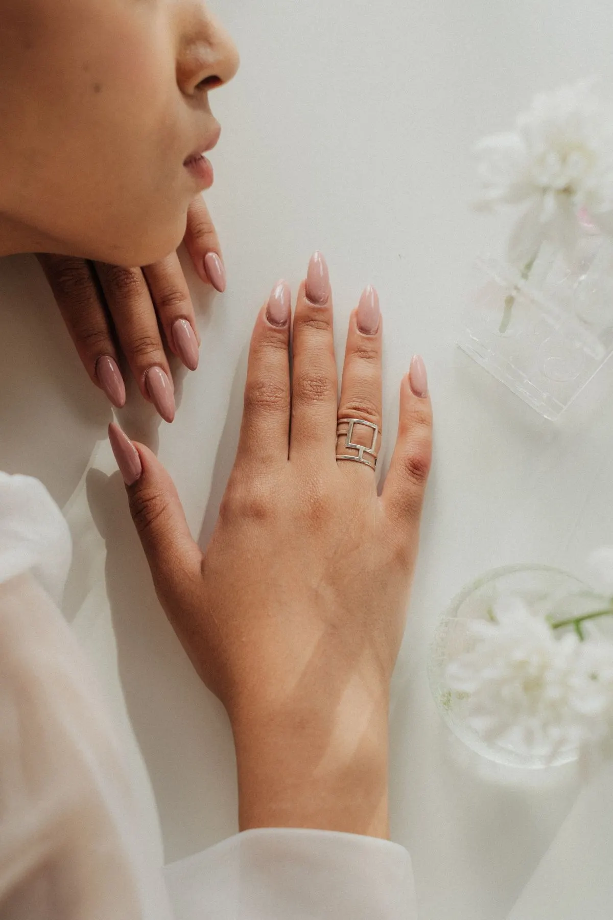 Mãos com unhas em tom nude, delicadas, sobre fundo claro com flores