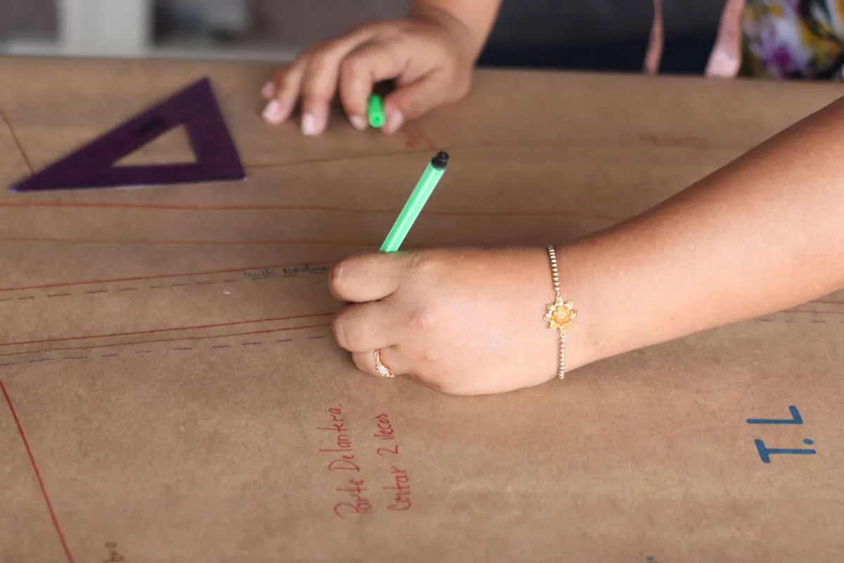 Mãos riscando um molde de costura em papel pardo